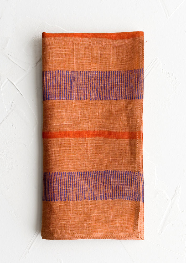 A terracotta linen napkin with block printed stripe design.