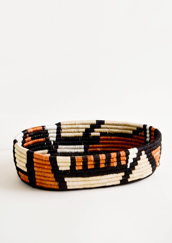 Oval shaped shallow bread basket made from woven natural grass in black and terracotta geometric print