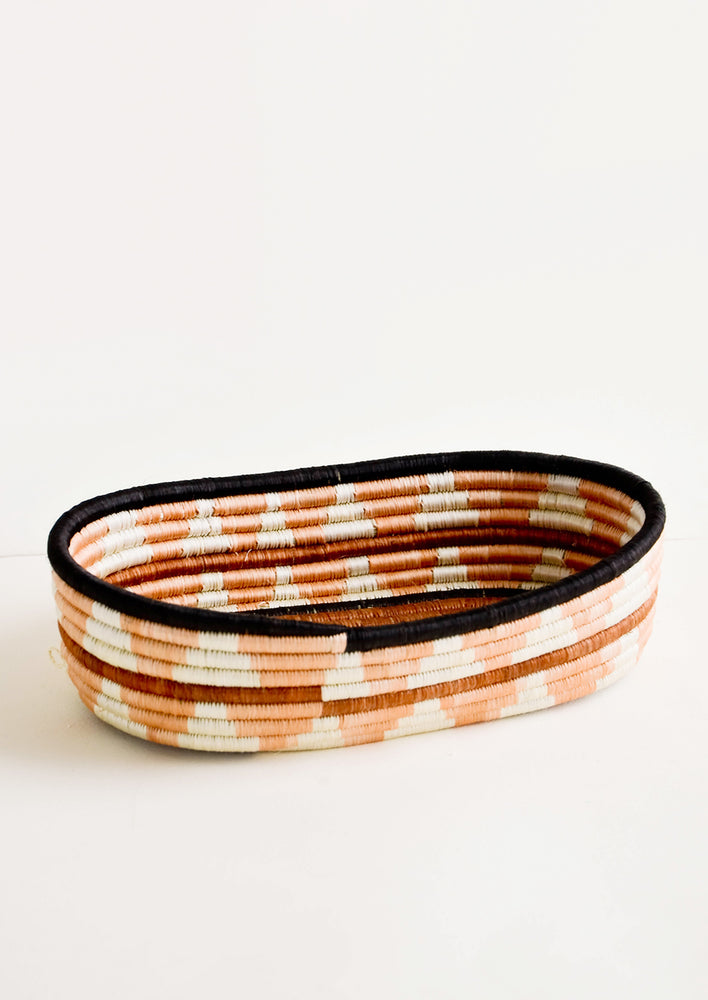 Oval shaped shallow bread basket made from woven natural grass in peachy geometric pattern