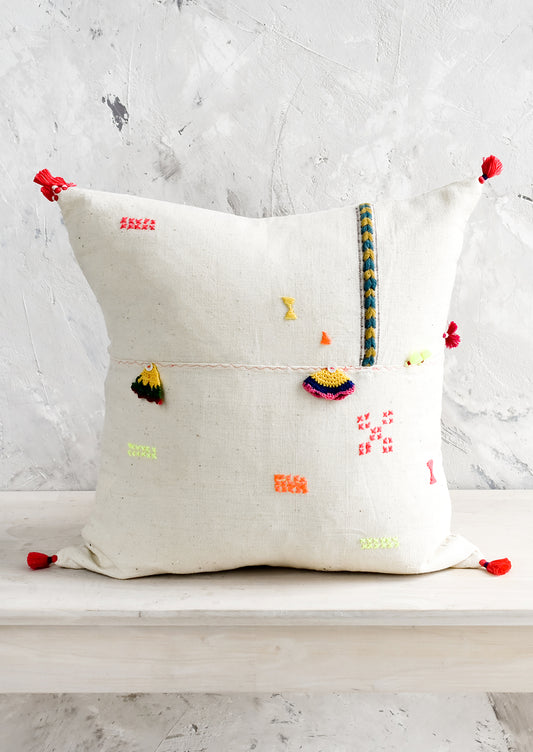A square throw pillow with neon embroidery and applique detailing.