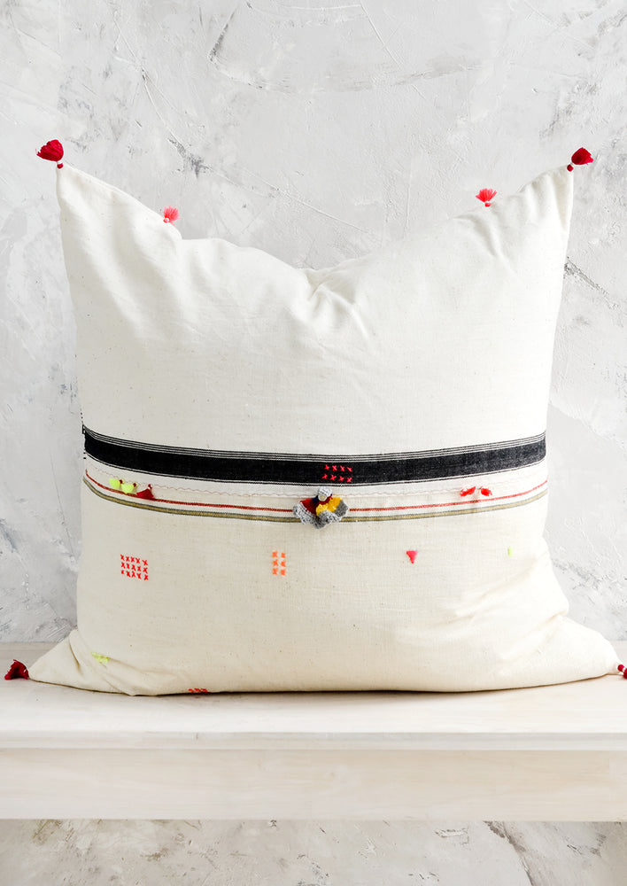 1: A square throw pillow with neon embroidery and tassel detailing.