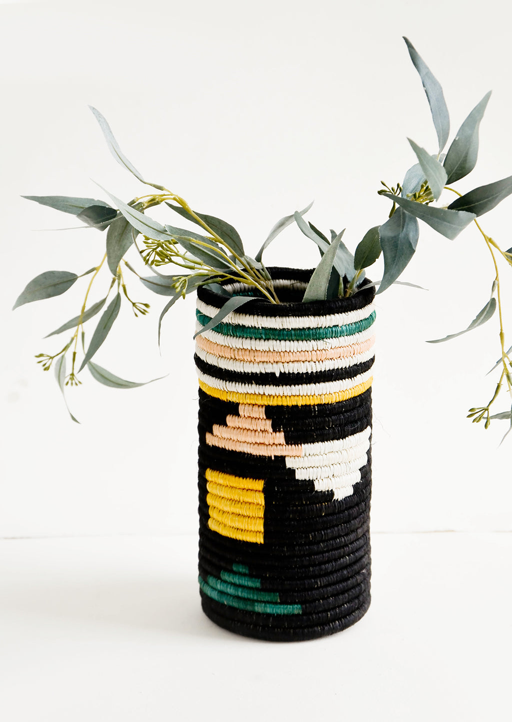 Black Geo Multi: Tall vases made of woven natural grass in colorful geometric pattern, with eucalyptus leaves inside
