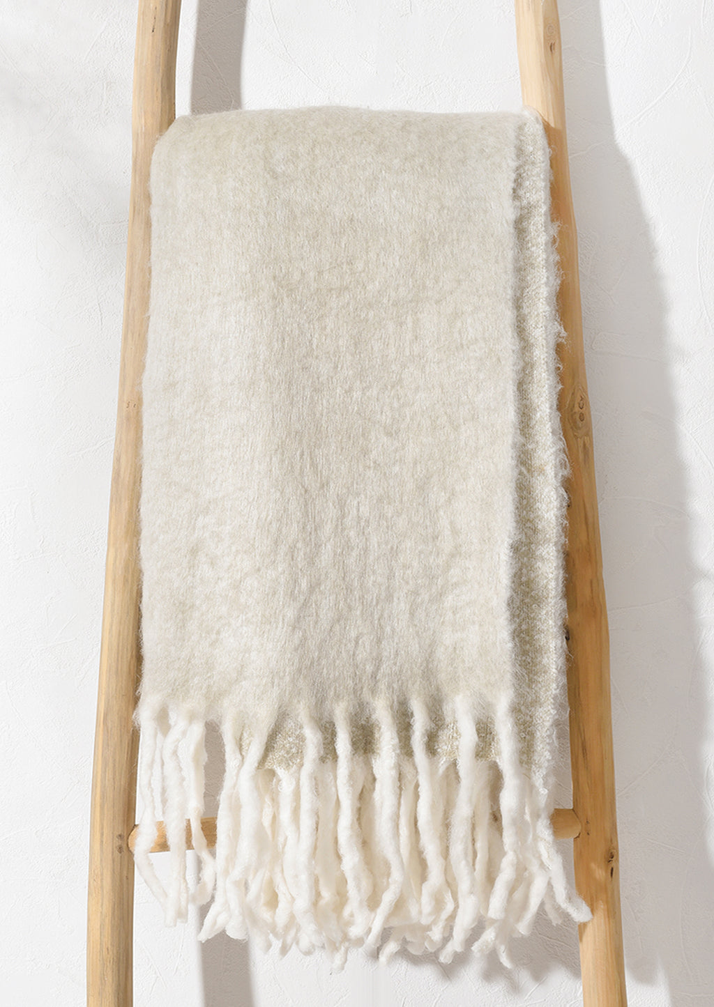 1: A beige mohair blanket hanging on a ladder.