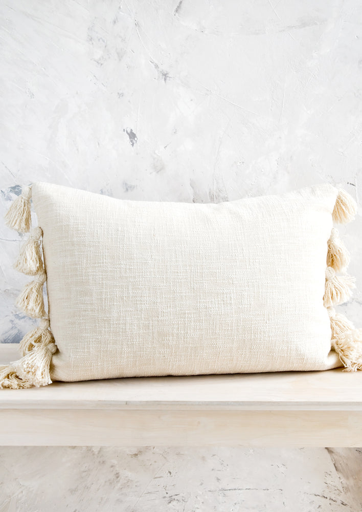 1: Lumbar throw pillow in textured, cream colored cotton with large decorative tassels at sides.
