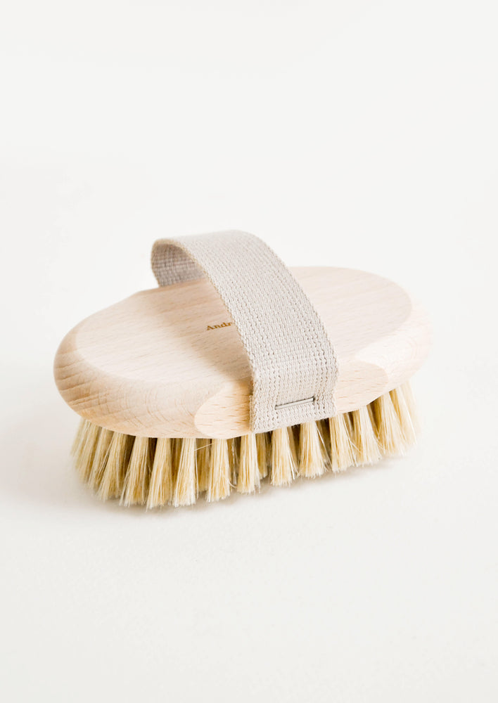 Massage Brush / Beech: An oval body brush in a light colored natural wood with a cotton hand strap.
