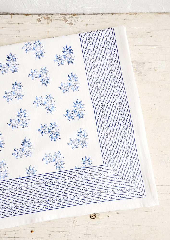White cotton tablecloth with blue floral print, folded on an antique table.