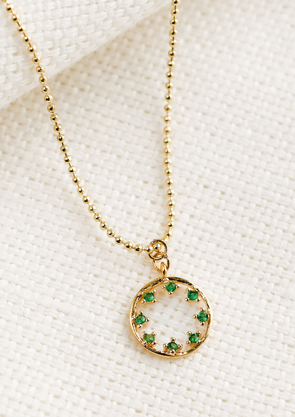 Emerald: A gold necklace with circular pendant with green inner stones.