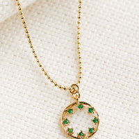 Emerald: A gold necklace with circular pendant with green inner stones.