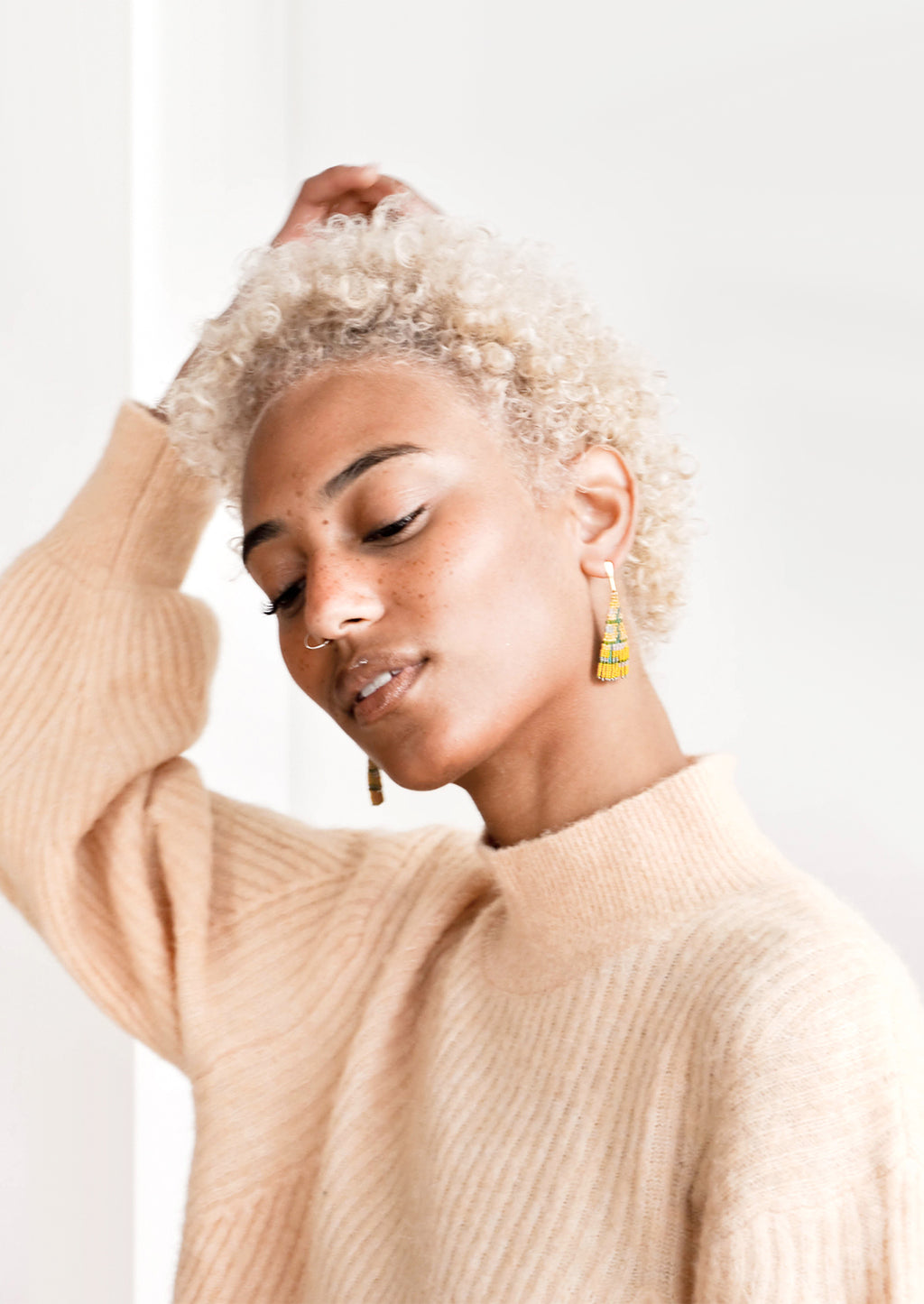 3: Model wears yellow triangle shaped beaded earrings and peach sweater.