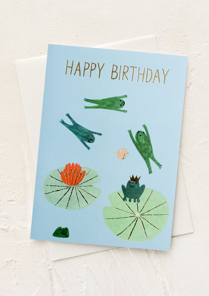 1: A greeting card with illustrated frogs jumping around on lilypads.
