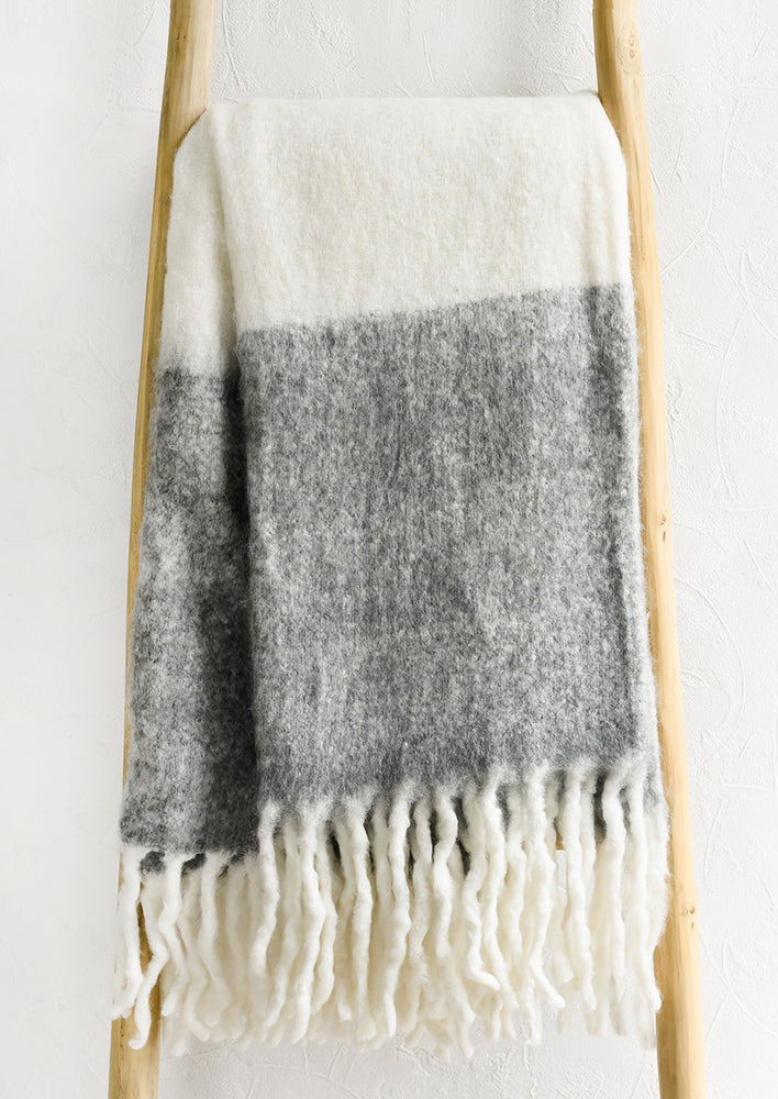 A mohair throw blanket in white and heather grey with long fringe trim.
