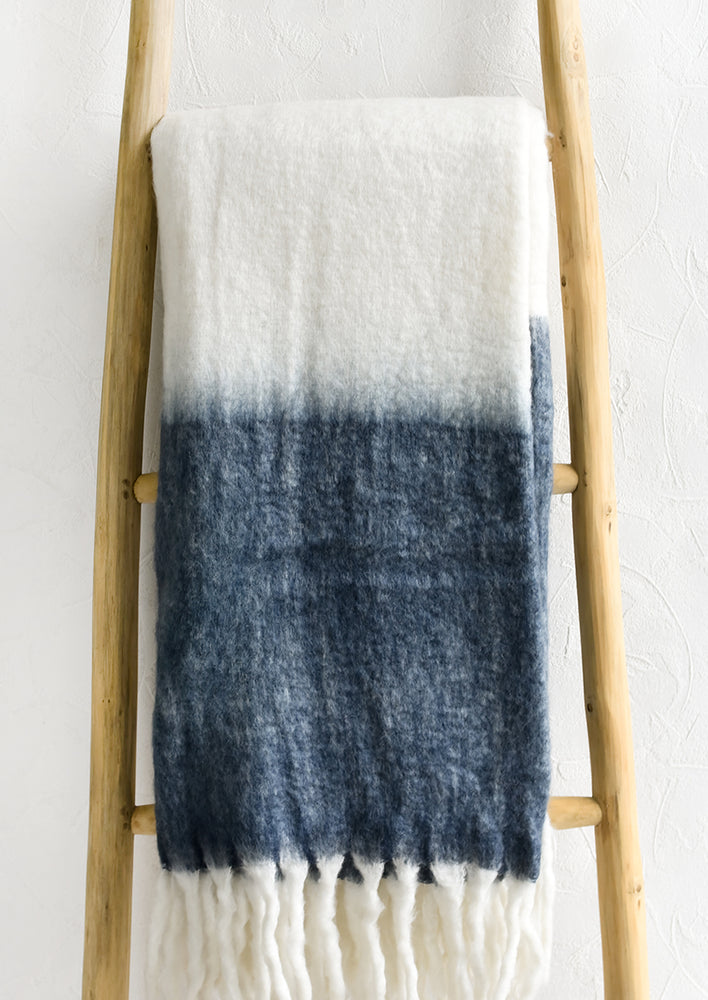 A mohair throw blanket in white and stone blue with long fringe trim.