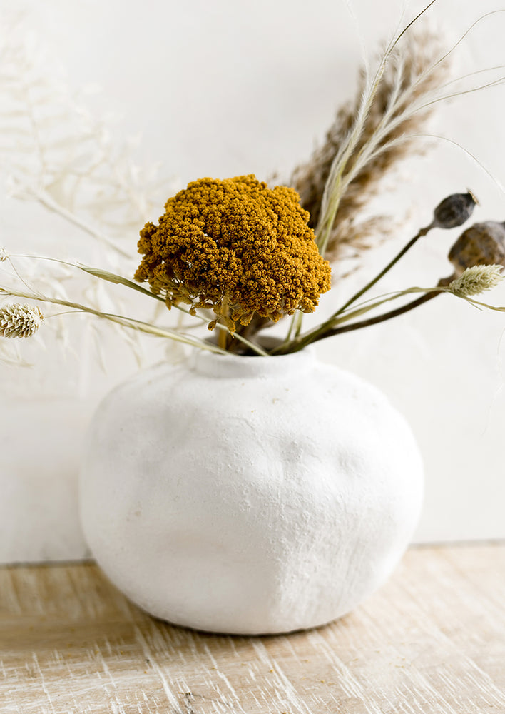 A white ceramic vase with dried flowers.