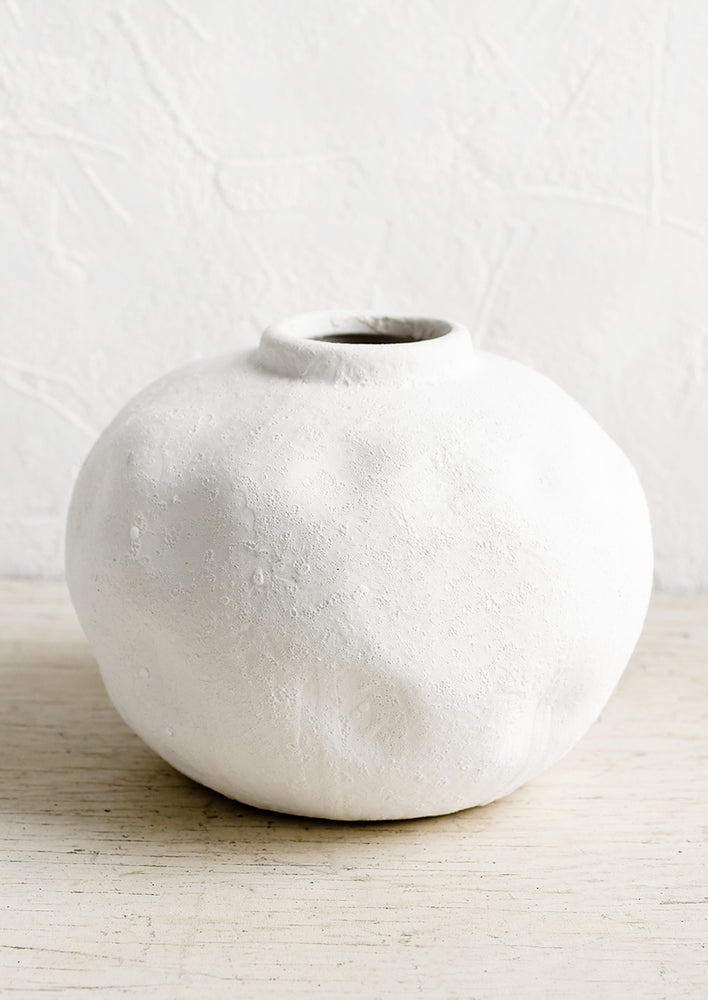 1: A white ceramic vase in round shape with plaster texture.