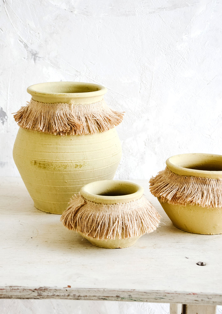 Three ochre clay vases in incremental sizes with fringed jute trim around opening