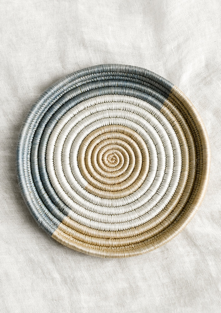A round, shallow sweetgrass tray in dusty blue, white and tan.