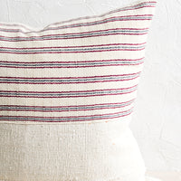 1: A throw pillow with top half in ivory, red and blue striped fabric and bottom half in natural mudcloth.