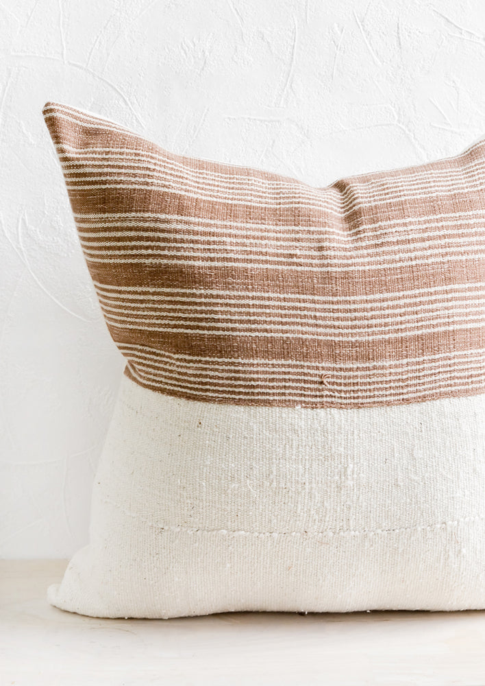 1: A throw pillow with top half in brown & ivory striped fabric and bottom half in natural mudcloth.