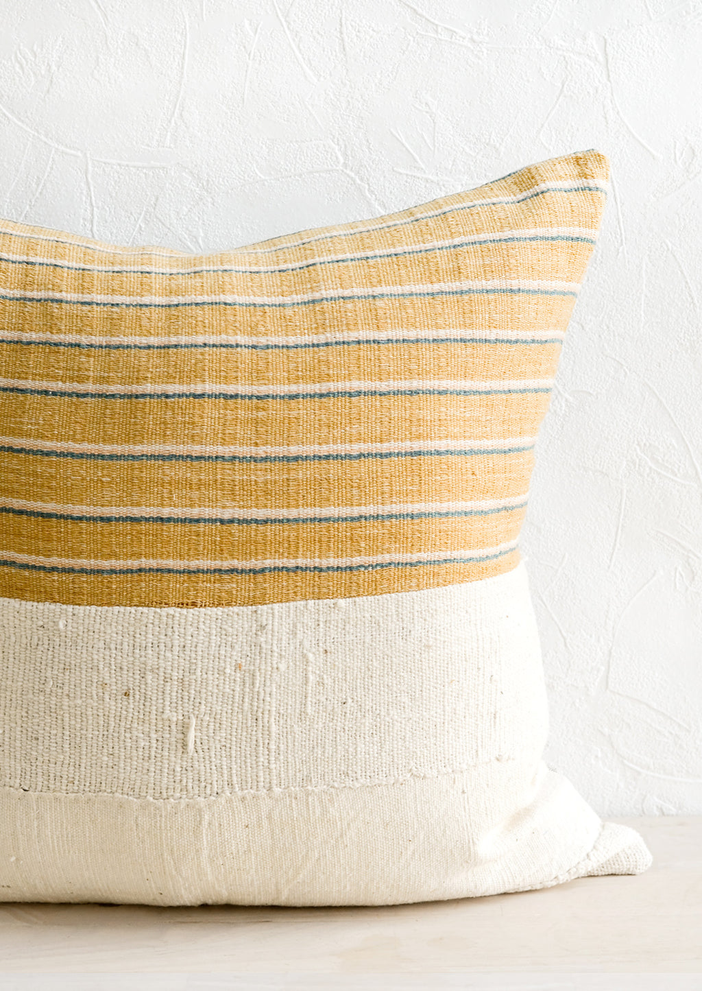 1: A throw pillow with top half in mustard, ivory & teal striped fabric and bottom half in natural mudcloth.