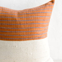 1: A throw pillow with top half in rust & indigo striped fabric and bottom half in natural mudcloth.