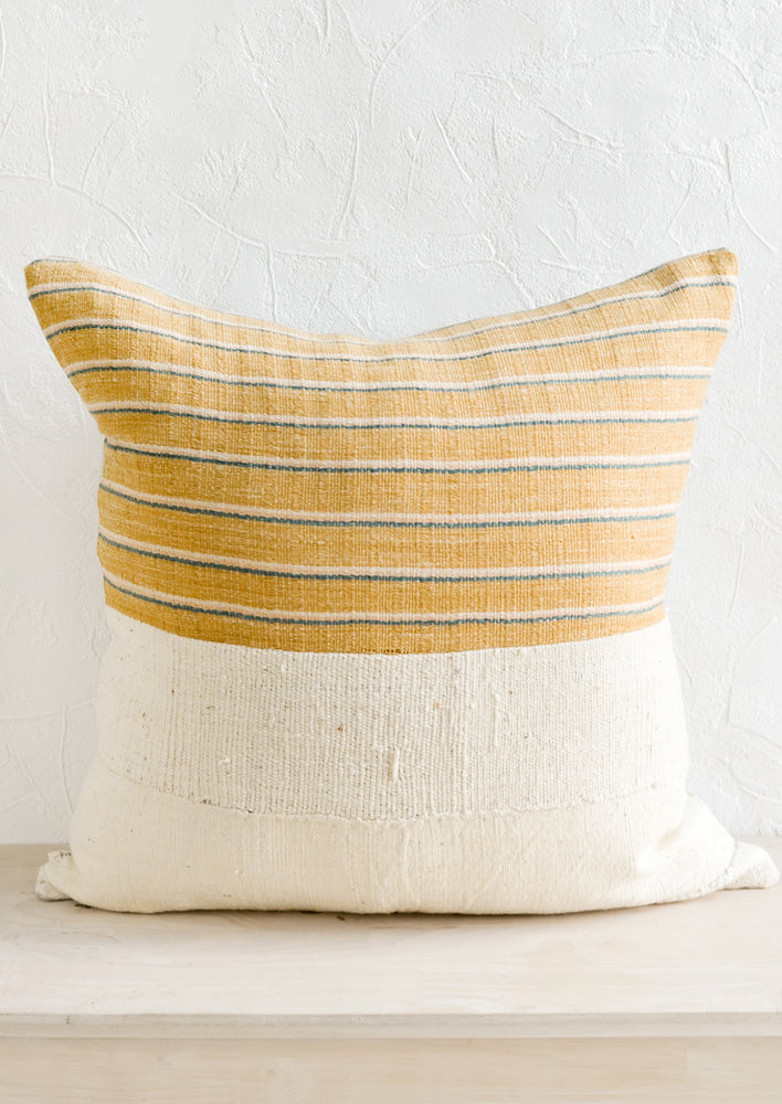2: A throw pillow with top half in mustard, ivory & teal striped fabric and bottom half in natural mudcloth.