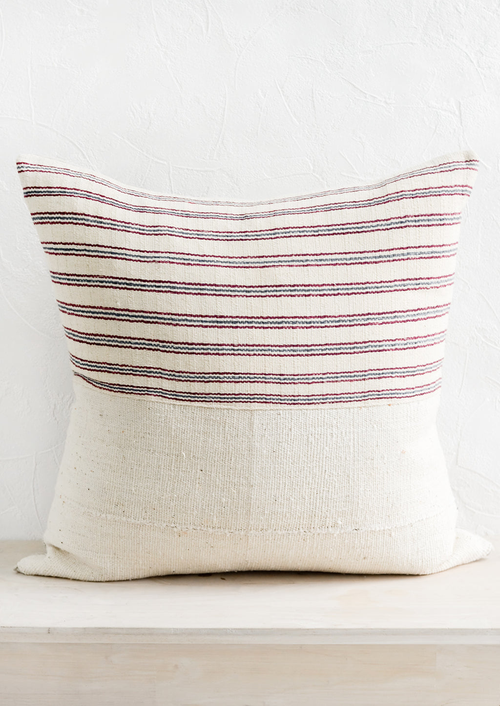2: A throw pillow with top half in ivory, red and blue striped fabric and bottom half in natural mudcloth.