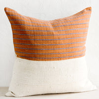 2: A throw pillow with top half in rust & indigo striped fabric and bottom half in natural mudcloth.