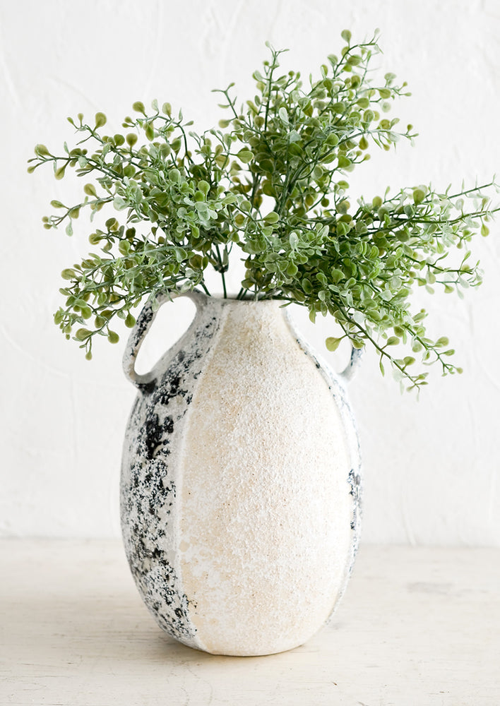 A distressed ceramic vase in tall shape with side handles, displaying green leafy plant.