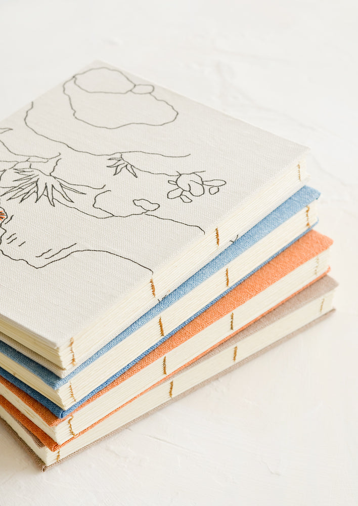 A stack of cloth journals with hand-bound seams.