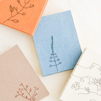 1: An array of cloth covered journals with botanical embroidery on covers.