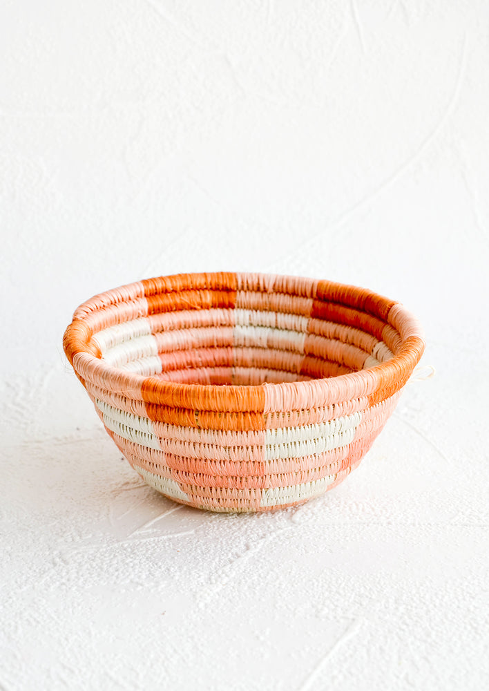 Small woven catchall bowl made from sweetgrass in a peach and terracotta geometric design.