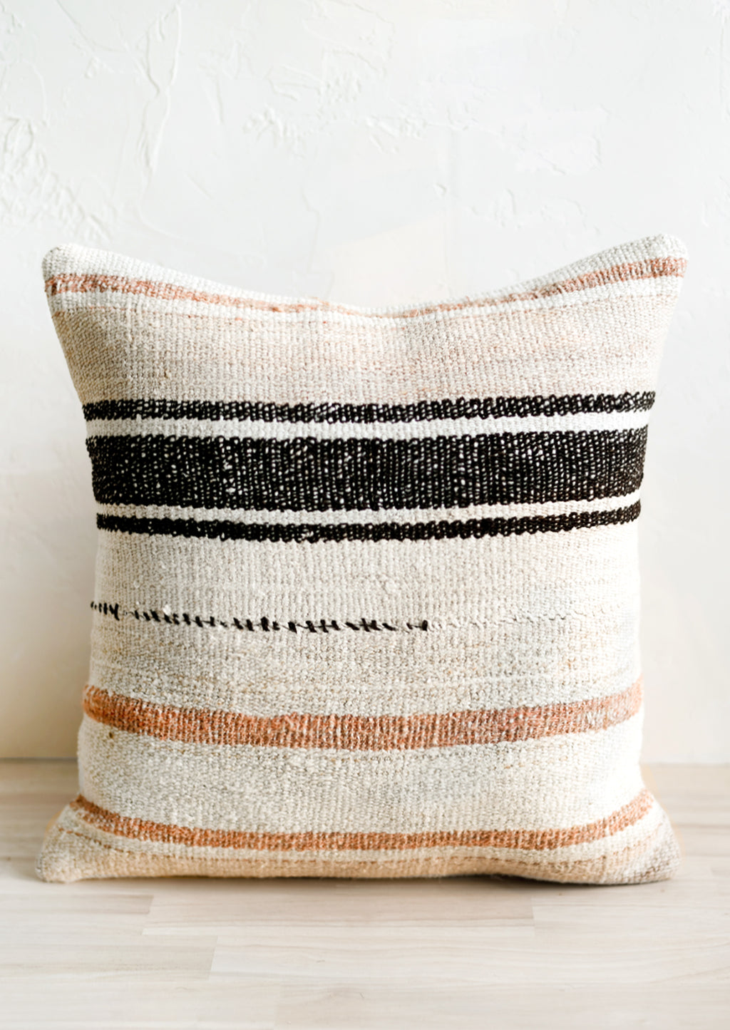 1: A square throw pillow in ivory with black and peach/clay stripes.