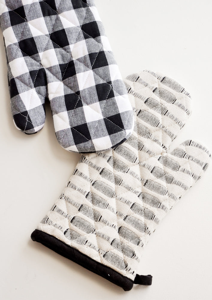 1: Two black and white oven mitts in buffalo check and stipe patterns.