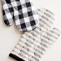 1: Two black and white oven mitts in buffalo check and stipe patterns.