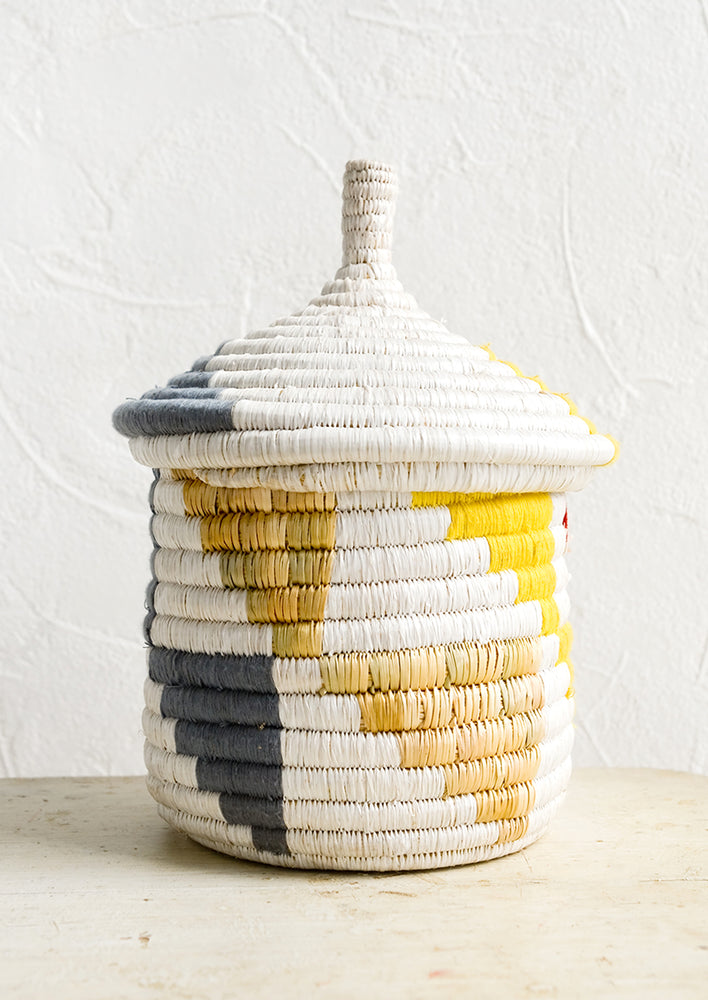 Small [$42.00]: A short woven basket with gourd-style lid in white with natural, yellow and blue-grey triangle pattern.