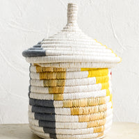 Small [$42.00]: A short woven basket with gourd-style lid in white with natural, yellow and blue-grey triangle pattern.