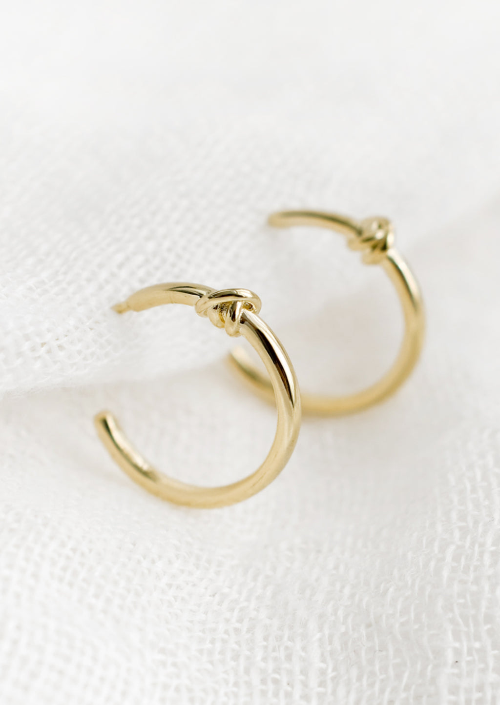 2: A pair of gold hoop earrings with single knot detail at top.