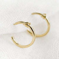 2: A pair of gold hoop earrings with single knot detail at top.
