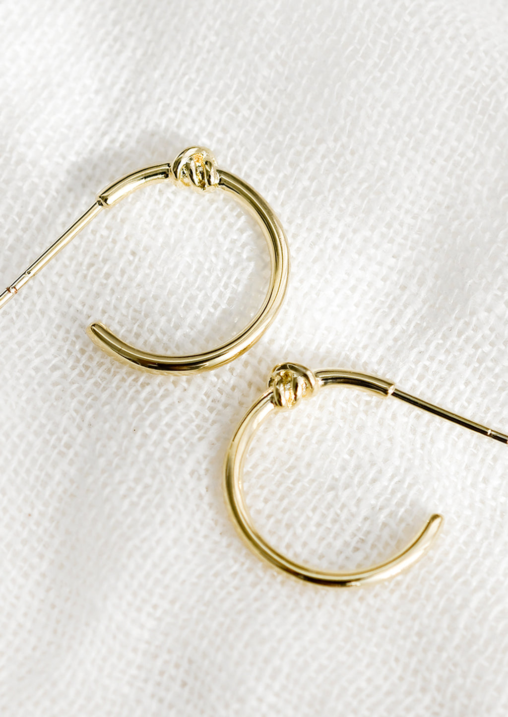 1: A pair of gold hoop earrings with single knot detail at top.