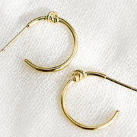 1: A pair of gold hoop earrings with single knot detail at top.