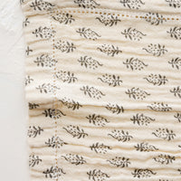 2: A dark grey floral motif on natural cotton gauze with hemstitch detail.