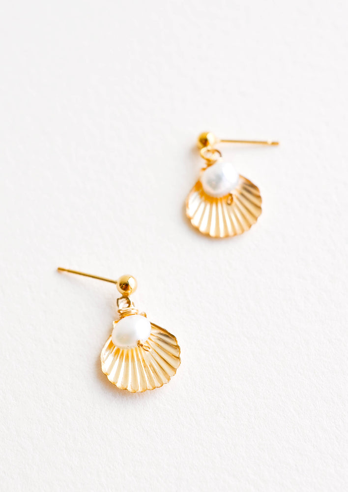 Dangling earring featuring gold shell charm paired with pearl bead, hanging from post.