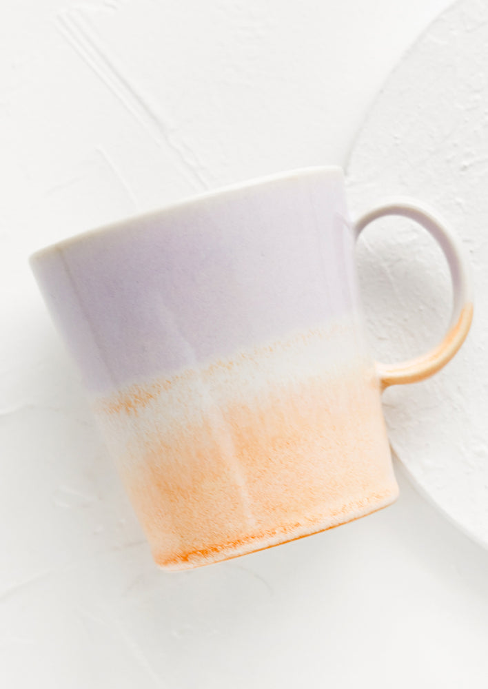 A ceramic coffee mug with handle in light purple and pastel orange.