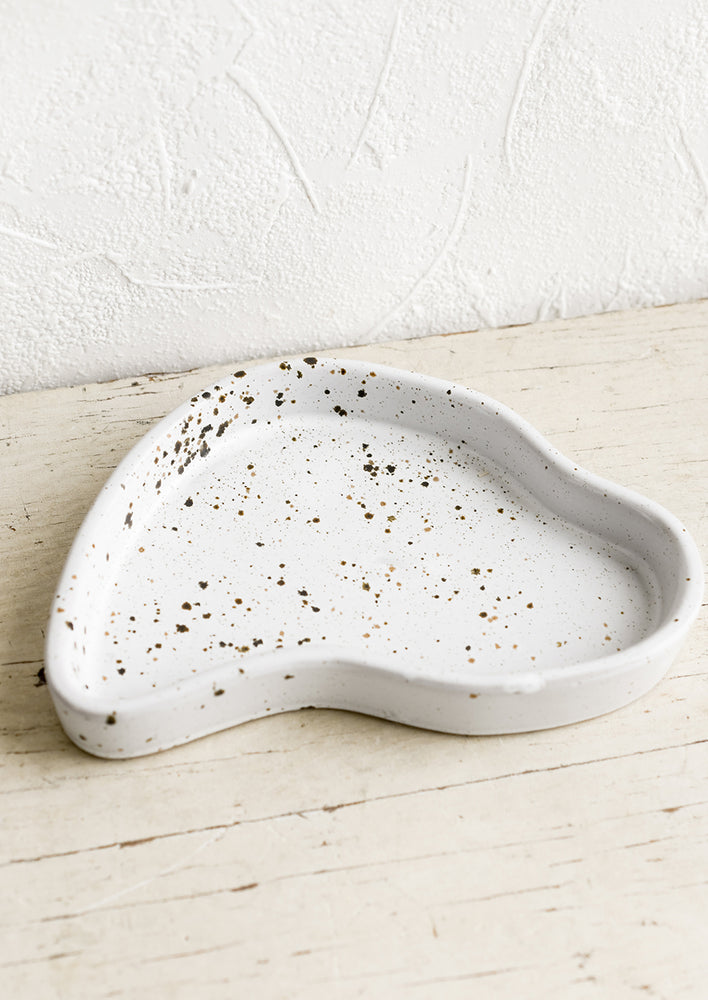 An asymmetrical small ceramic tray in white glaze with brown speckles.