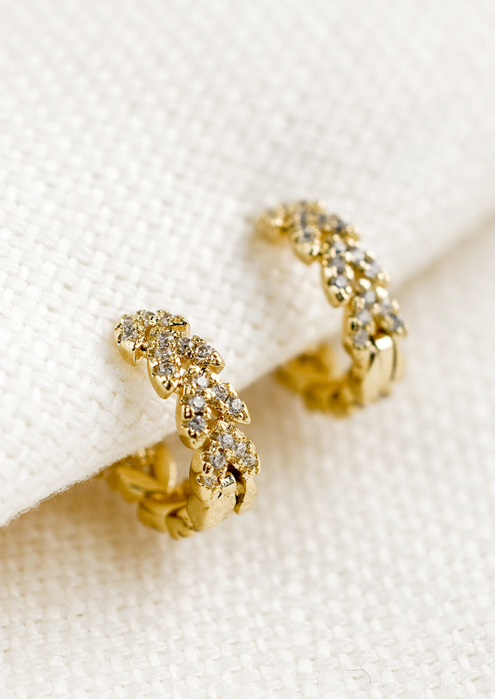 1: A pair of gold huggie hoop earrings with clear crystal laurel leaf design.