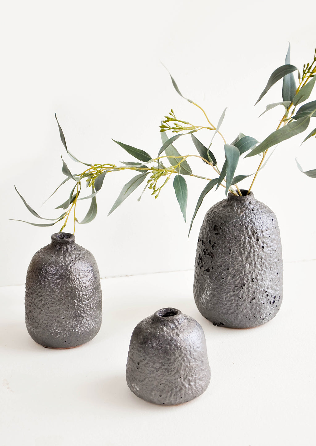 2: Group shot of heavily textured ceramic bud vases in dark metallic grey, styled with eucalyptus stem - LEIF