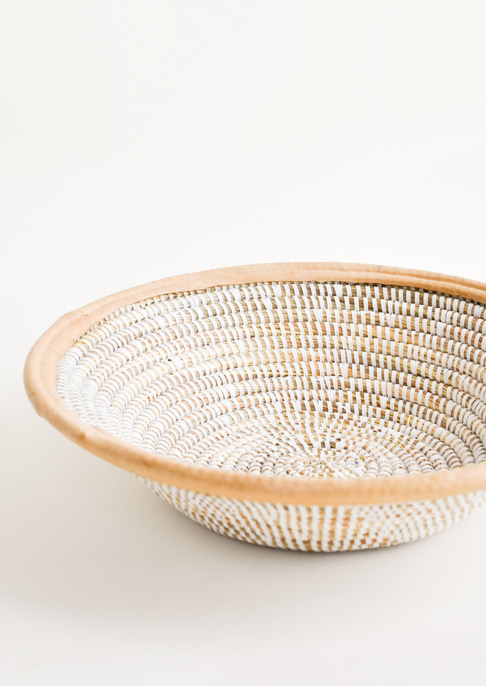 A woven seagrass and white plastic bowl with leather trim around top.