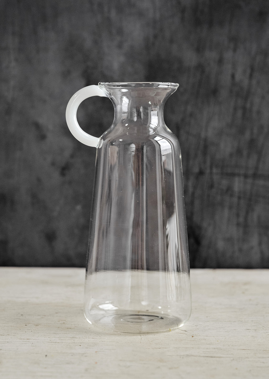 Medium: A clear glass vase in milk bottle shape with white handle at one side.