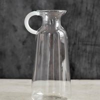 Medium: A clear glass vase in milk bottle shape with white handle at one side.