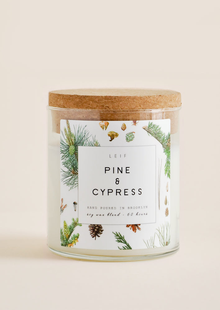 Pine & Cypress: A glass candle with a cork lid and white botanical printed label reading "pine and cypress."